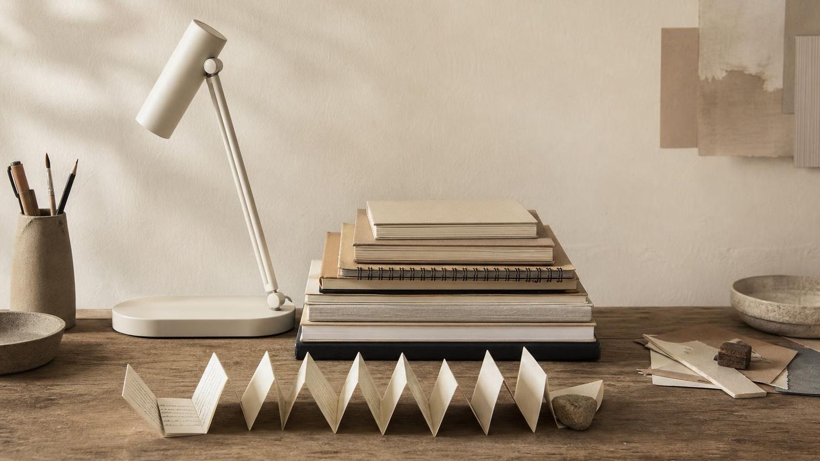 An empty desk with stacked notebooks, a closed lamp, and a row of folded notes
