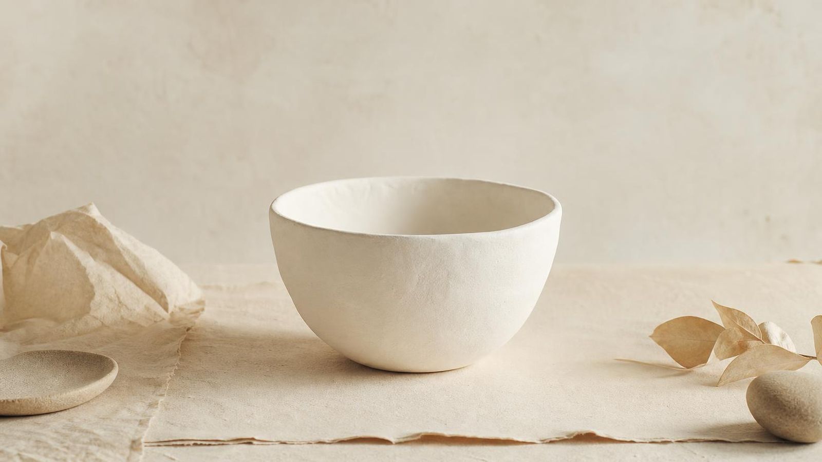 A plain white bowl on a paper-toned surface with minimal objects beside it